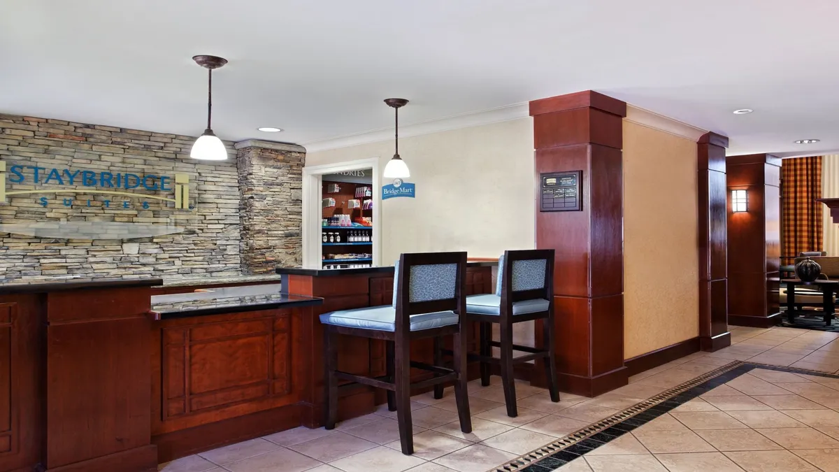 A warmly lit reception area featuring a modern stone wall, sleek bar stools, and guests checking in. The inviting design and welcoming staff set the tone for a family-friendly stay and hint at the amenities and hospitality provided throughout the property.