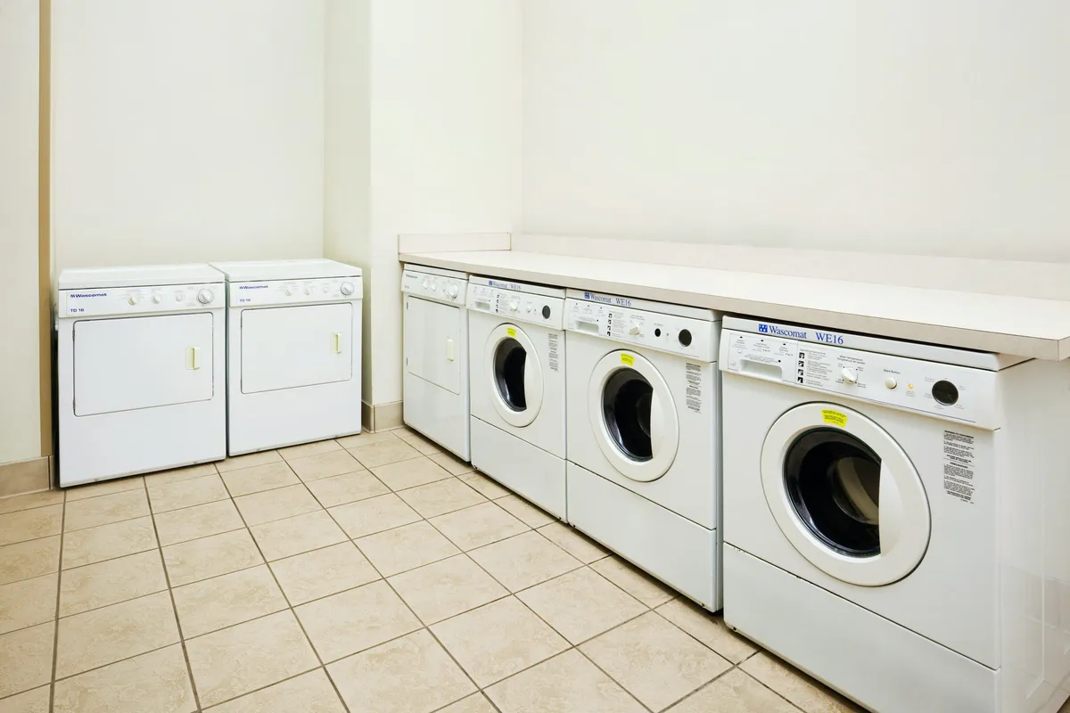 A practical laundry area equipped with multiple washing machines, a dryer, and a countertop for sorting and folding clothes. The space is clean and organized, supporting efficient laundry routines for guests.