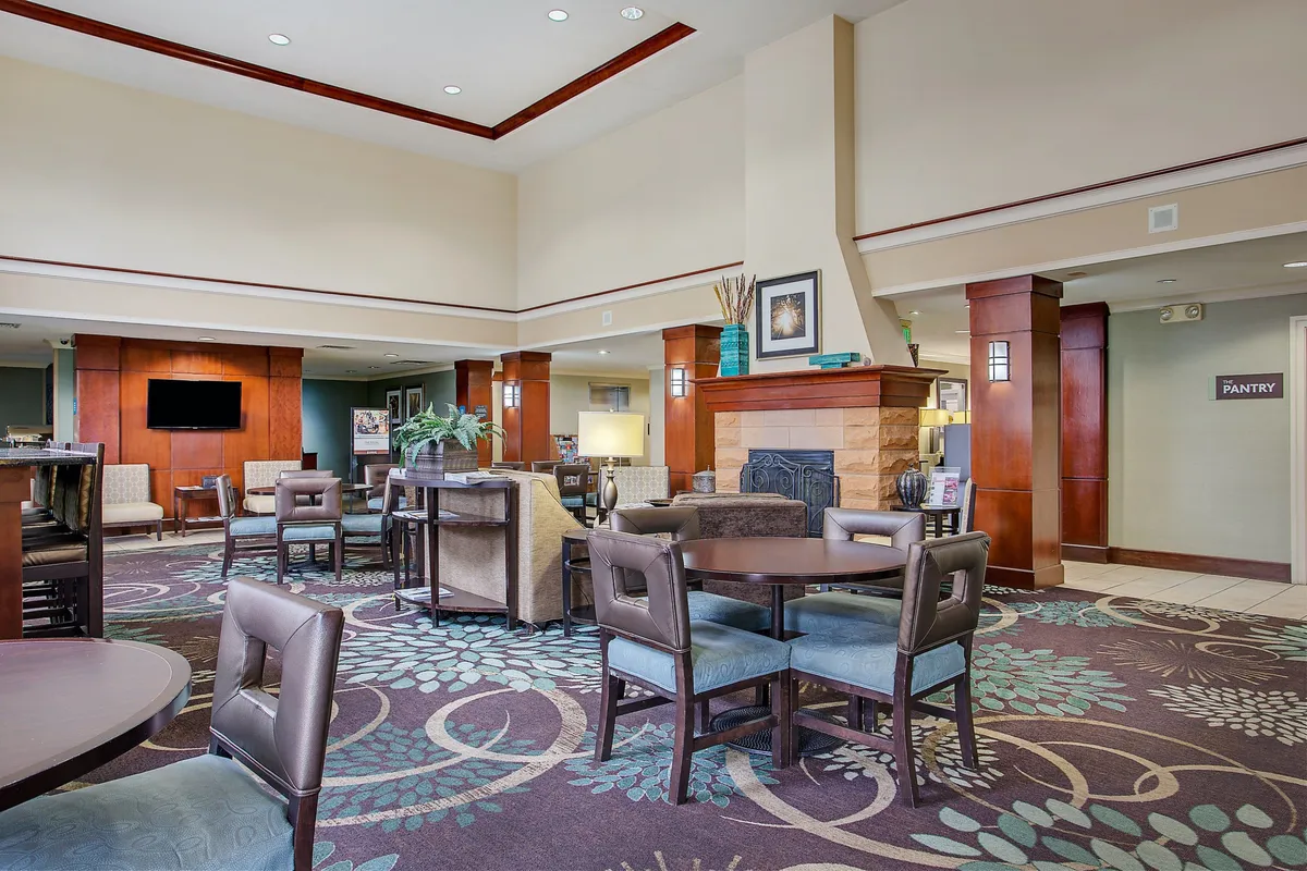 A cozy and inviting interior lounge features a glowing fireplace, plush seating, decorative plants, and a 'pantry' sign. The setting is ideal for guests to gather, relax, or enjoy a snack, mirroring the comfort offered after a day spent exploring outdoors.