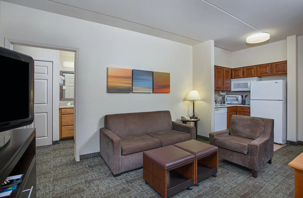 The image showcases a bright, inviting condo interior with a plush sofa set against tasteful wall art and a well-equipped kitchenette. The space looks perfect for unwinding after a day out, sharing meals, or cozy movie nights, all in a comfortable, contemporary setting.
