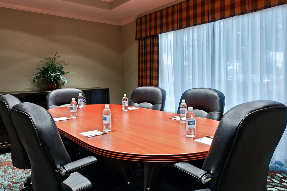 A modern conference room featuring a large conference table surrounded by sleek black leather chairs. The table is set with notepads and water bottles, creating a professional environment suited for meetings, brainstorming sessions, or team discussions. The overall ambiance is focused and businesslike, with ample lighting and minimal distractions.